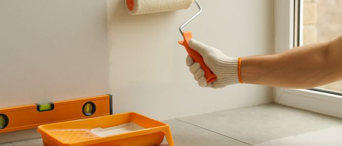 Application de peinture murale avec rouleau orange et matériaux de revêtement posés au sol
