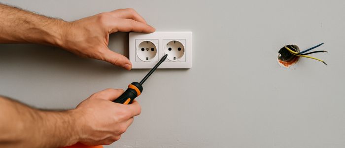Électricien en train d’installer une prise double avec outils et câbles apparents